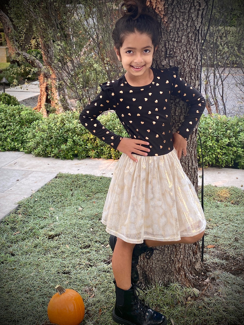 Young girl wearing a black and beige outfit next to a pumpkin