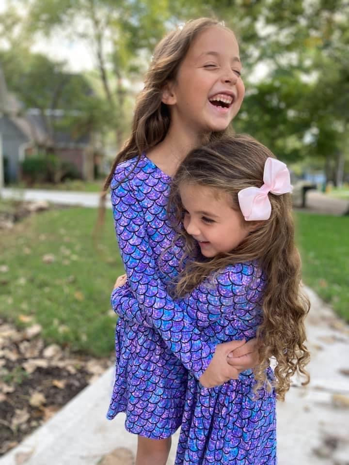 Young girl hugging her sister while wearing a matching blue dress.