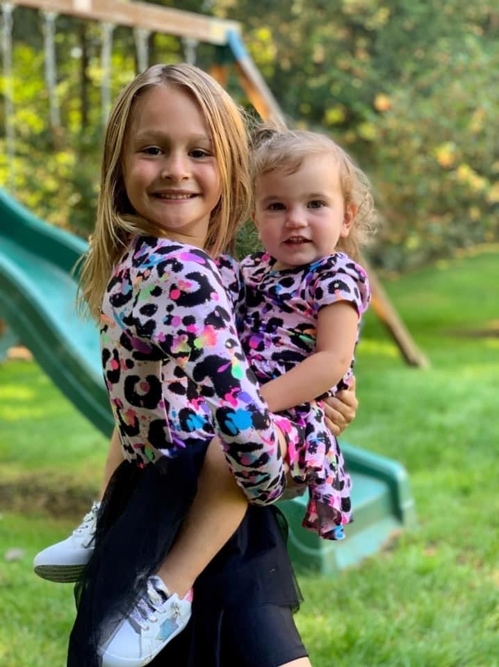 Young girl and a baby girl wearing matching outfit.