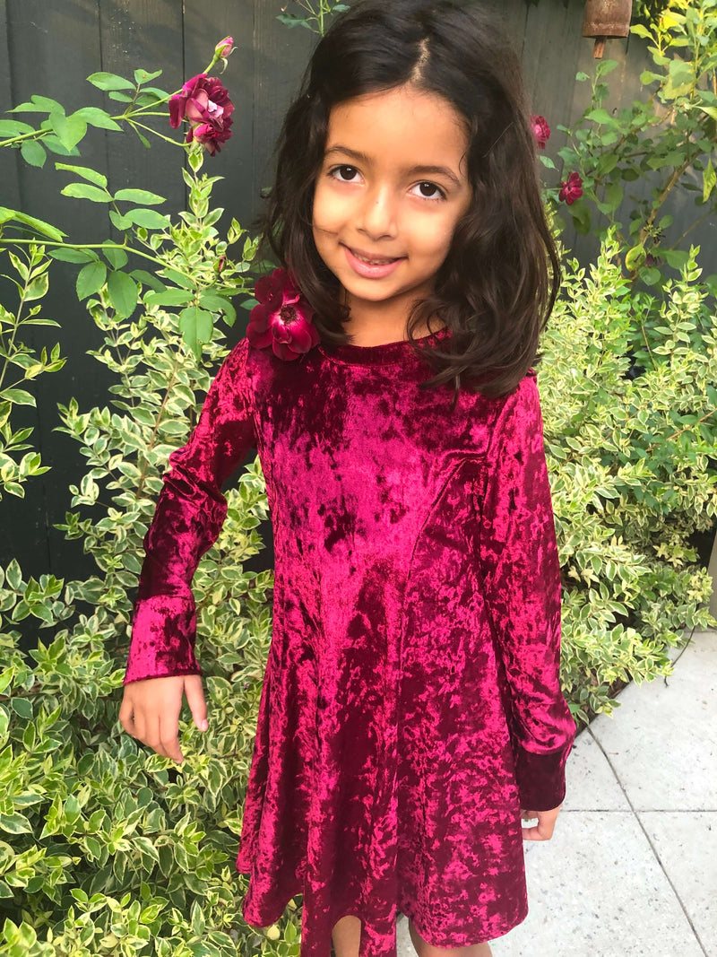 Young girl wearing a velvety red dress in front of a Christmas tree